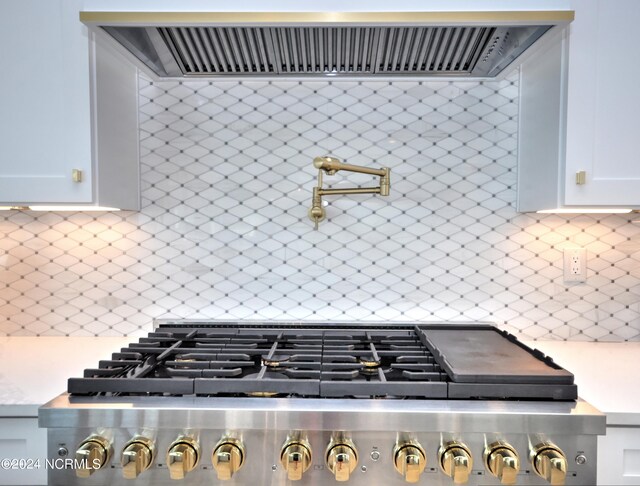 room details with wall chimney exhaust hood, white cabinetry, stainless steel stove, and tasteful backsplash