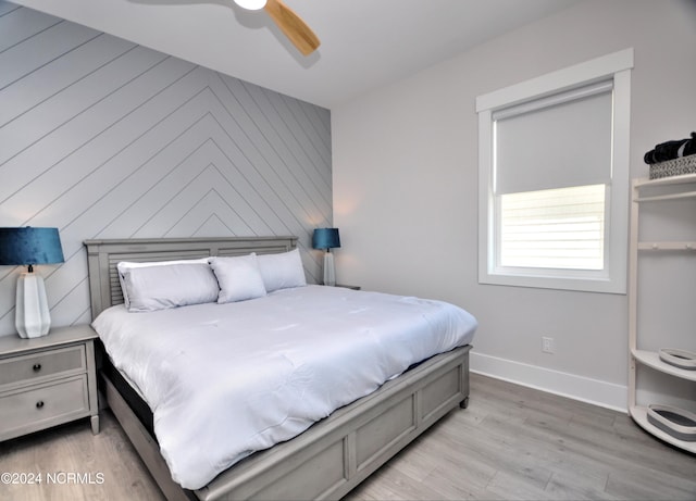 bedroom featuring ceiling fan, wood walls, light wood-type flooring, and baseboards