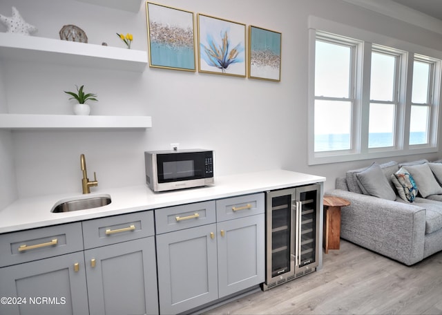 bar featuring wine cooler, a sink, and light wood-style flooring