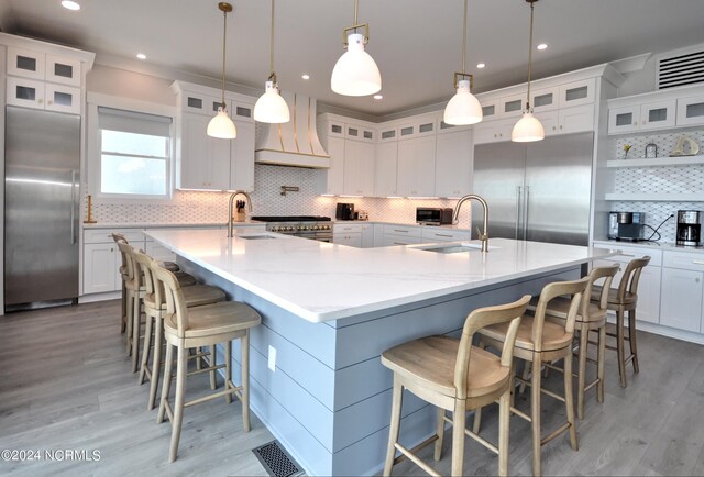 kitchen with high end appliances, custom range hood, a large island with sink, and a sink