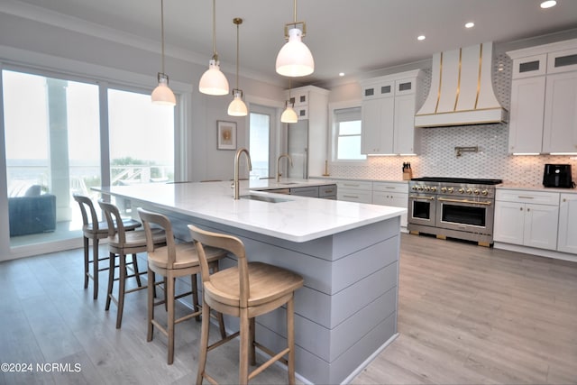 kitchen featuring a large island, sink, hanging light fixtures, custom range hood, and range with two ovens