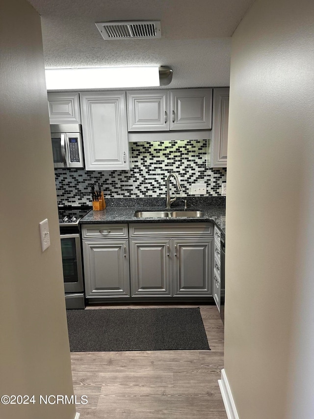 kitchen with light hardwood / wood-style flooring, appliances with stainless steel finishes, tasteful backsplash, sink, and gray cabinets