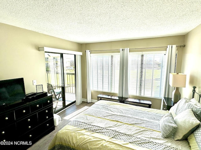 bedroom featuring access to exterior, a textured ceiling, and wood finished floors