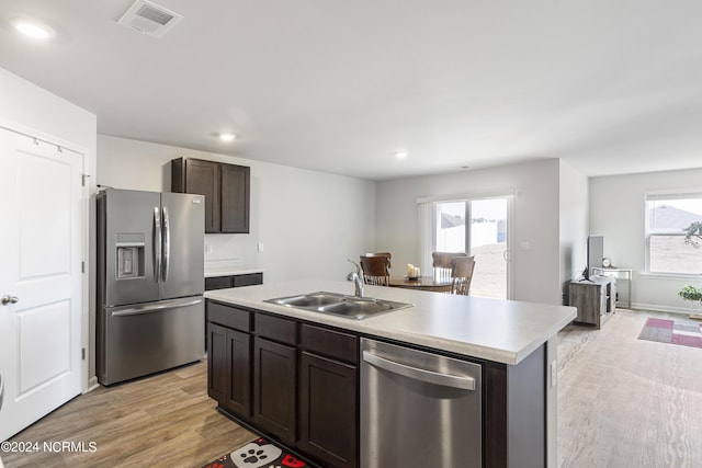 kitchen with sink, dark brown cabinets, stainless steel appliances, light hardwood / wood-style floors, and an island with sink