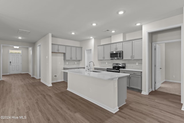 kitchen with appliances with stainless steel finishes, gray cabinetry, sink, a center island with sink, and hardwood / wood-style flooring