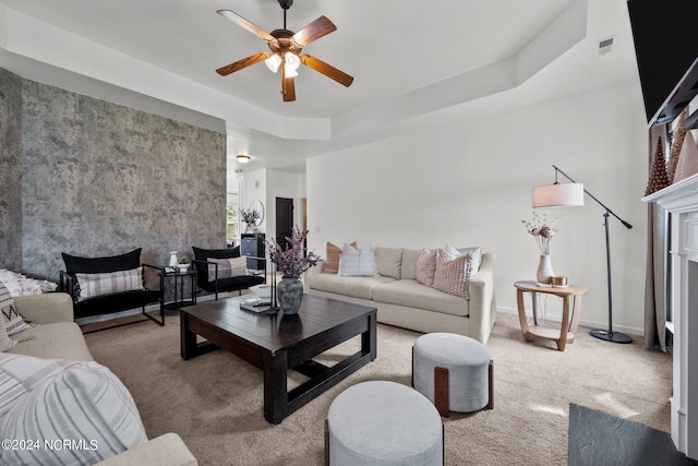 carpeted living room with ceiling fan, a tray ceiling, a fireplace, and baseboards