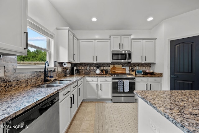 kitchen with appliances with stainless steel finishes, light stone countertops, sink, and white cabinets