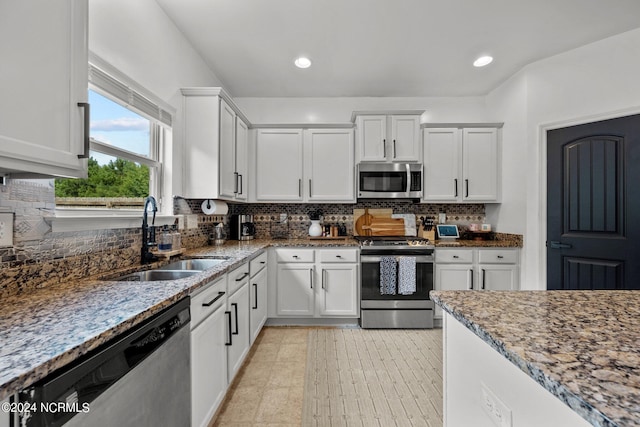 kitchen with stainless steel appliances, a sink, white cabinets, and light stone countertops