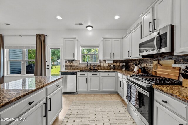 kitchen featuring appliances with stainless steel finishes, dark stone countertops, backsplash, and white cabinetry