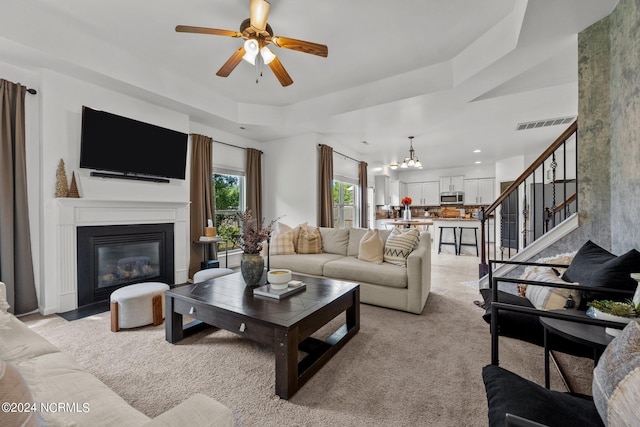 living area with stairs, visible vents, a fireplace with flush hearth, light carpet, and ceiling fan with notable chandelier