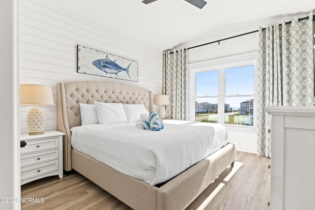 bedroom with ceiling fan, light wood-style flooring, vaulted ceiling, and wood walls