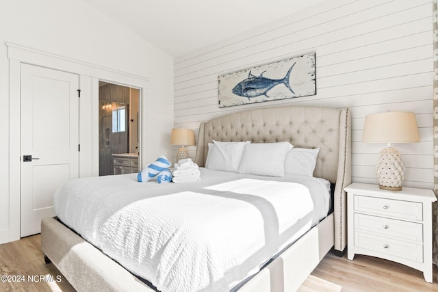 bedroom featuring connected bathroom, vaulted ceiling, light wood-style flooring, and wooden walls