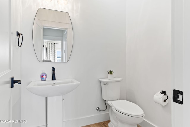 half bath with baseboards, toilet, and wood finished floors