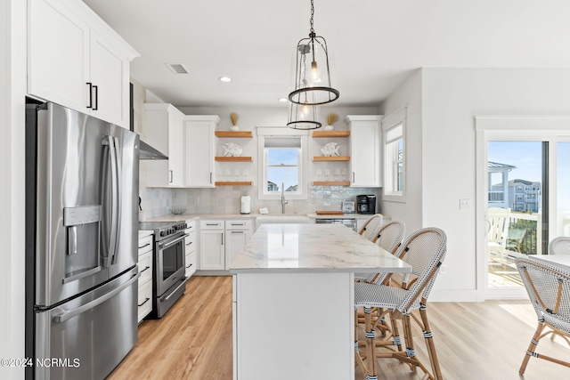 kitchen with a breakfast bar, white cabinets, appliances with stainless steel finishes, backsplash, and open shelves