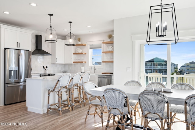 kitchen featuring white cabinets, light wood-style floors, appliances with stainless steel finishes, wall chimney range hood, and open shelves