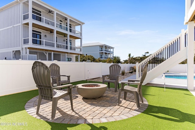 view of patio with a fenced backyard, ceiling fan, a fire pit, and a balcony