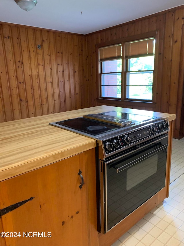 kitchen featuring light tile patterned floors, black stove, and wooden walls