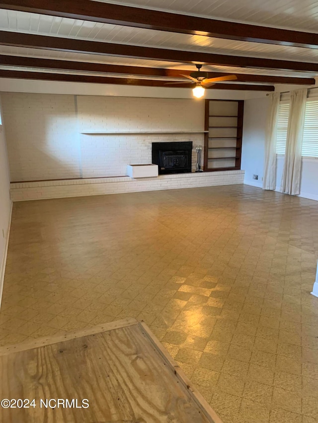 unfurnished living room with a brick fireplace, beam ceiling, and ceiling fan