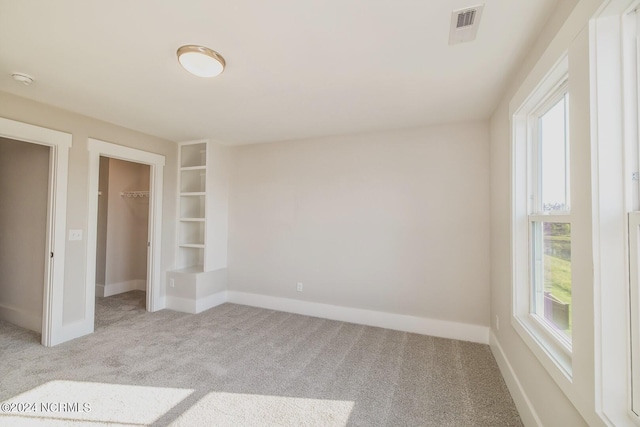 unfurnished bedroom featuring multiple windows, light carpet, a closet, and a spacious closet