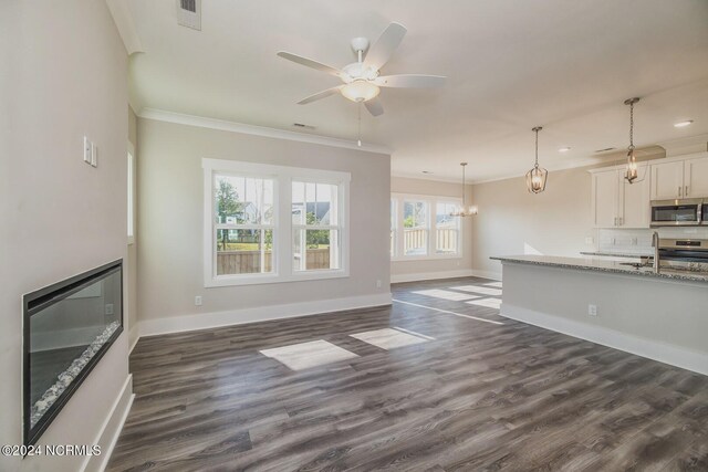 unfurnished living room featuring sink, ceiling fan with notable chandelier, dark hardwood / wood-style flooring, and crown molding