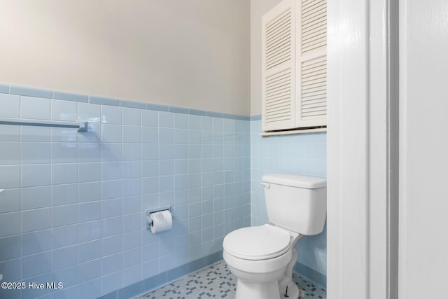 bathroom with wainscoting, tile walls, and toilet