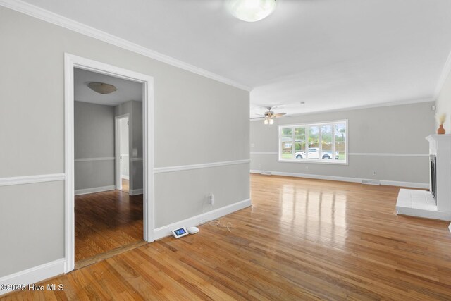 unfurnished living room featuring baseboards, light wood-type flooring, a ceiling fan, a fireplace, and crown molding