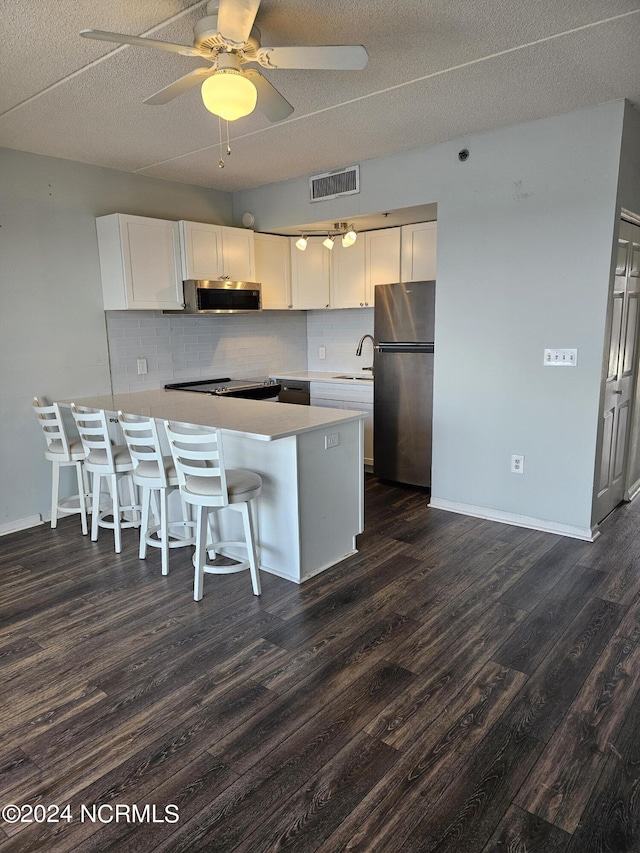 kitchen with a breakfast bar area, stainless steel appliances, visible vents, white cabinetry, and a peninsula