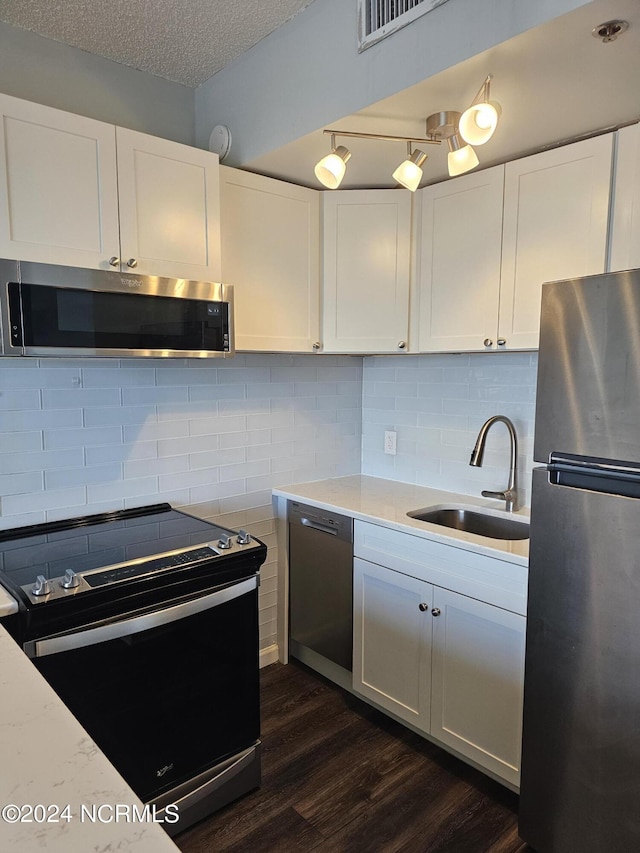 kitchen with tasteful backsplash, white cabinets, appliances with stainless steel finishes, a textured ceiling, and a sink