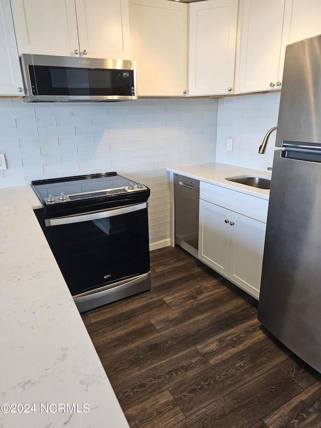 kitchen with dark wood finished floors, tasteful backsplash, appliances with stainless steel finishes, white cabinets, and a sink