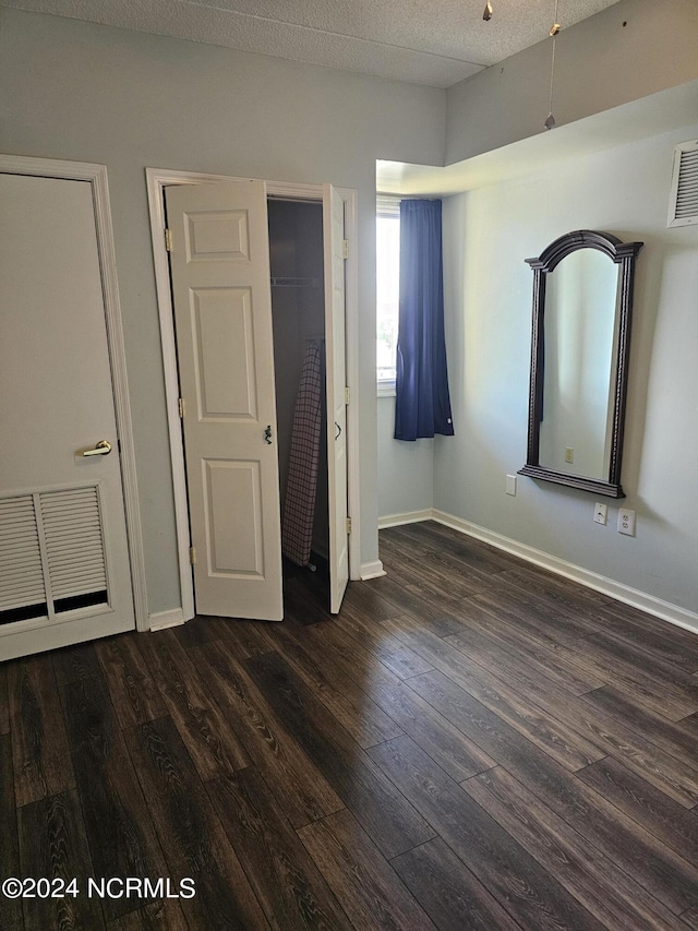 unfurnished bedroom featuring a textured ceiling, dark wood-type flooring, and baseboards