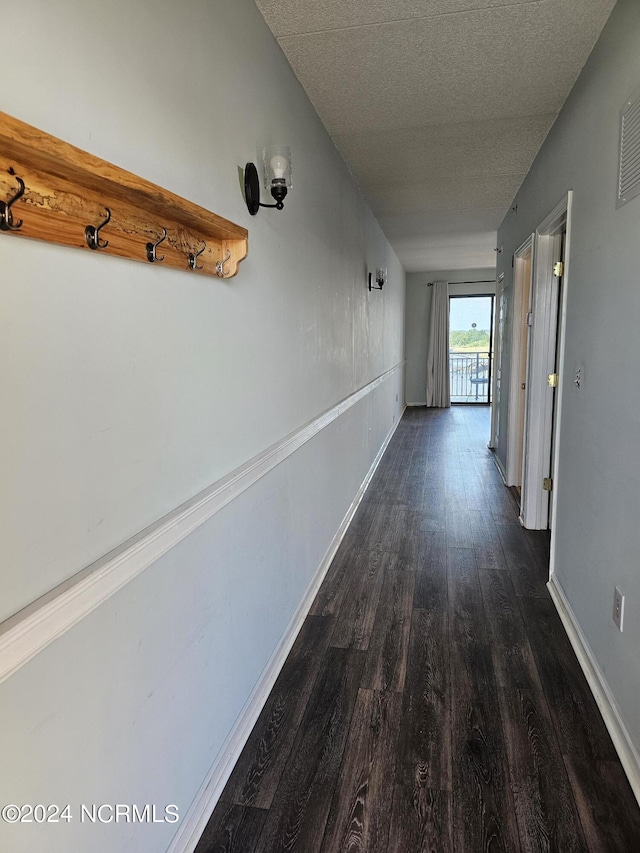 corridor with dark wood-style flooring, a textured ceiling, and baseboards