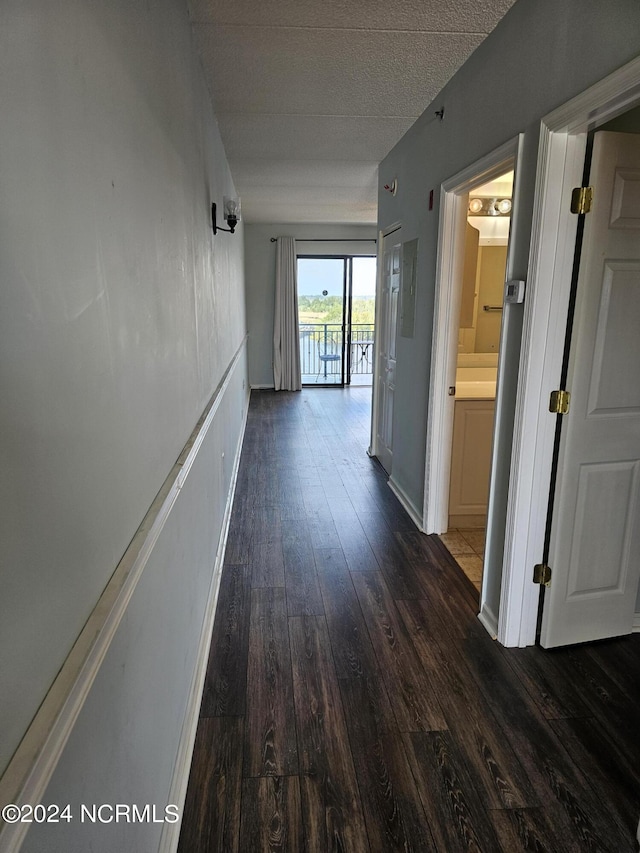 hall featuring a textured ceiling, dark wood-type flooring, and baseboards