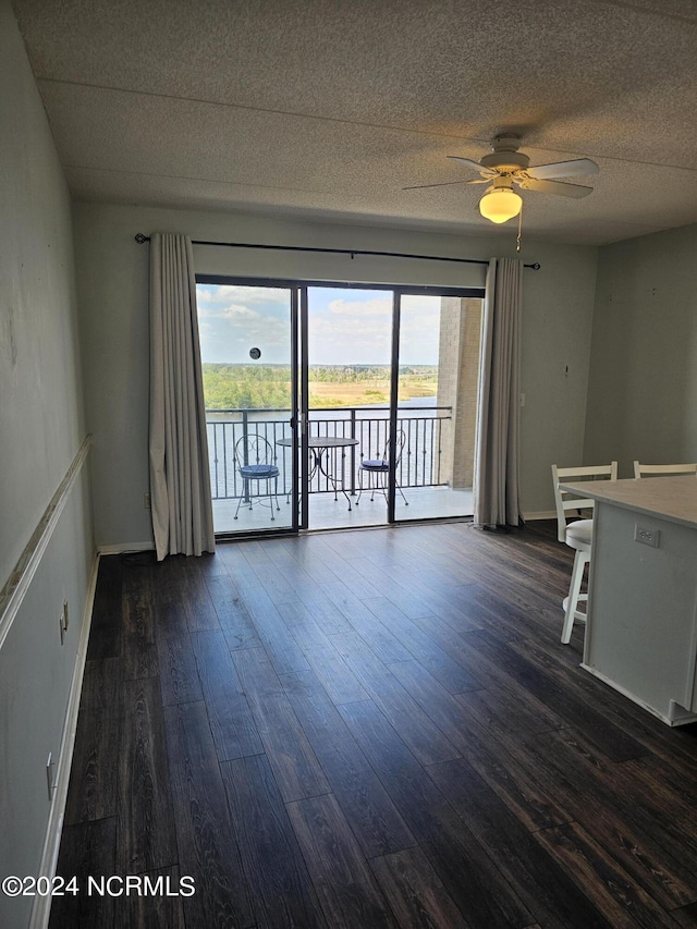 unfurnished living room featuring dark wood-style flooring, a healthy amount of sunlight, a textured ceiling, and baseboards