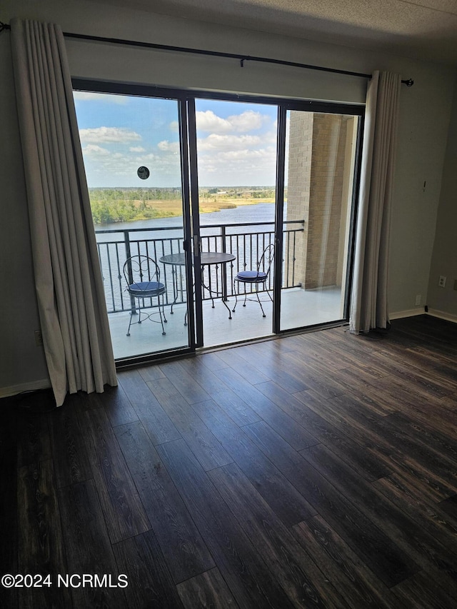 empty room featuring a water view, a textured ceiling, baseboards, and dark wood-style flooring