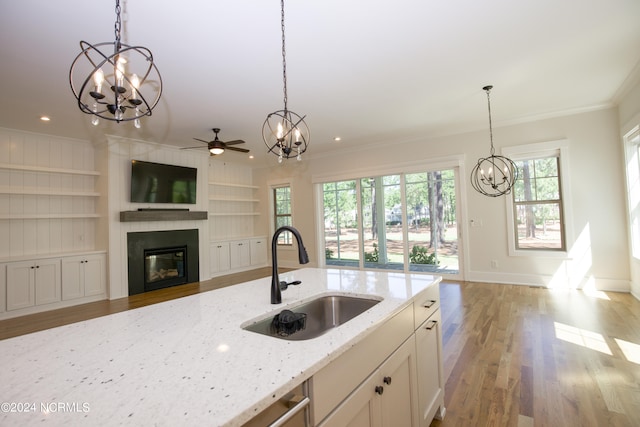 kitchen with ceiling fan with notable chandelier, light stone counters, hanging light fixtures, and sink