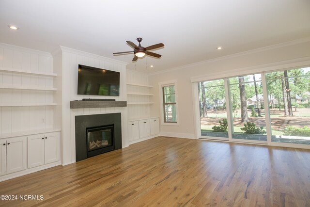 unfurnished living room featuring built in shelves, a large fireplace, ornamental molding, light hardwood / wood-style flooring, and ceiling fan