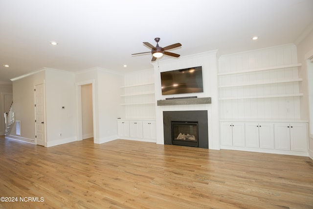 unfurnished living room featuring a fireplace, ornamental molding, built in features, ceiling fan, and light hardwood / wood-style floors