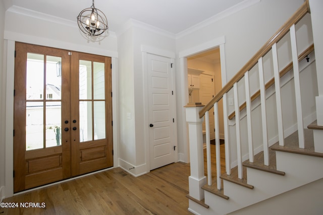 foyer entrance featuring hardwood / wood-style flooring, ornamental molding, a chandelier, and french doors