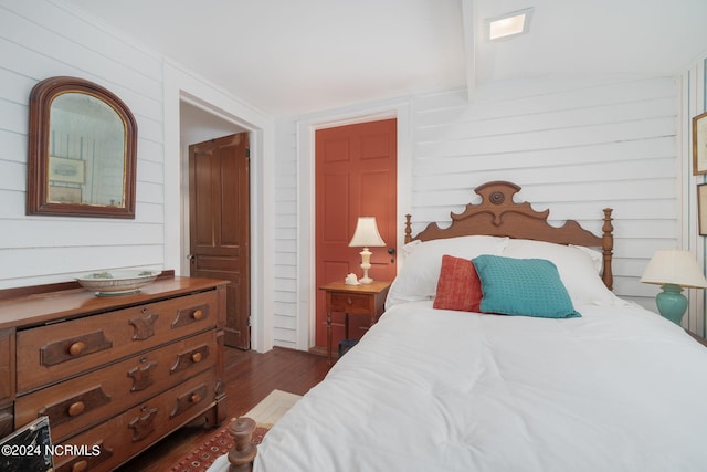 bedroom with dark wood-type flooring and wood walls