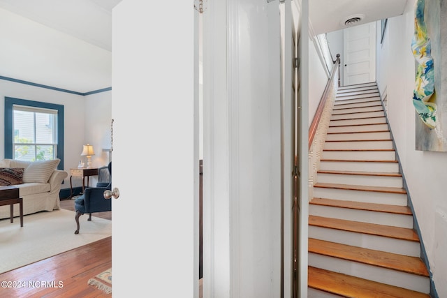 stairway with crown molding and wood-type flooring