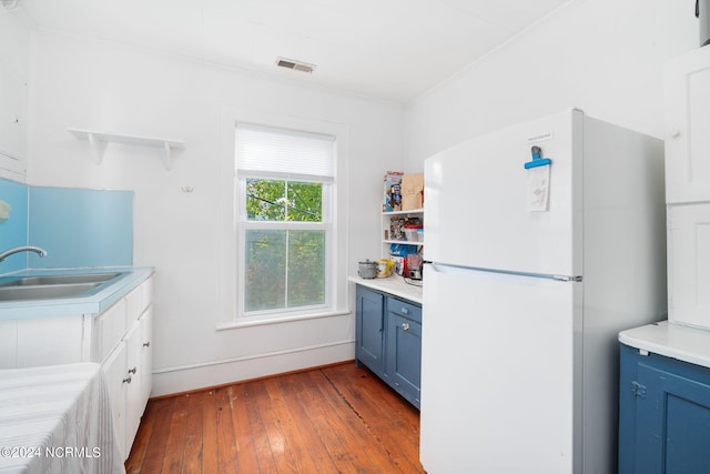 kitchen featuring blue cabinets, dark hardwood / wood-style floors, crown molding, white fridge, and sink