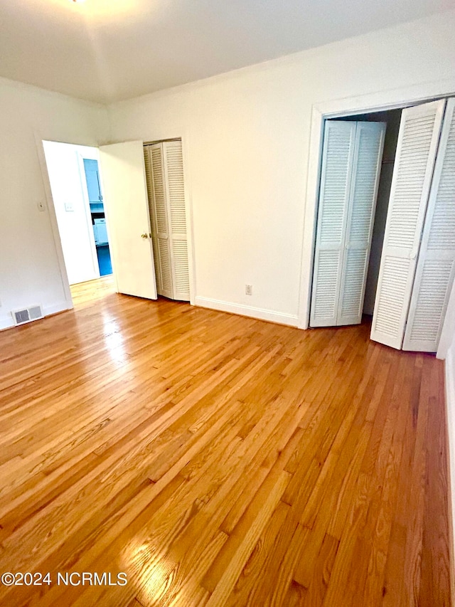 unfurnished bedroom with light hardwood / wood-style floors and multiple closets