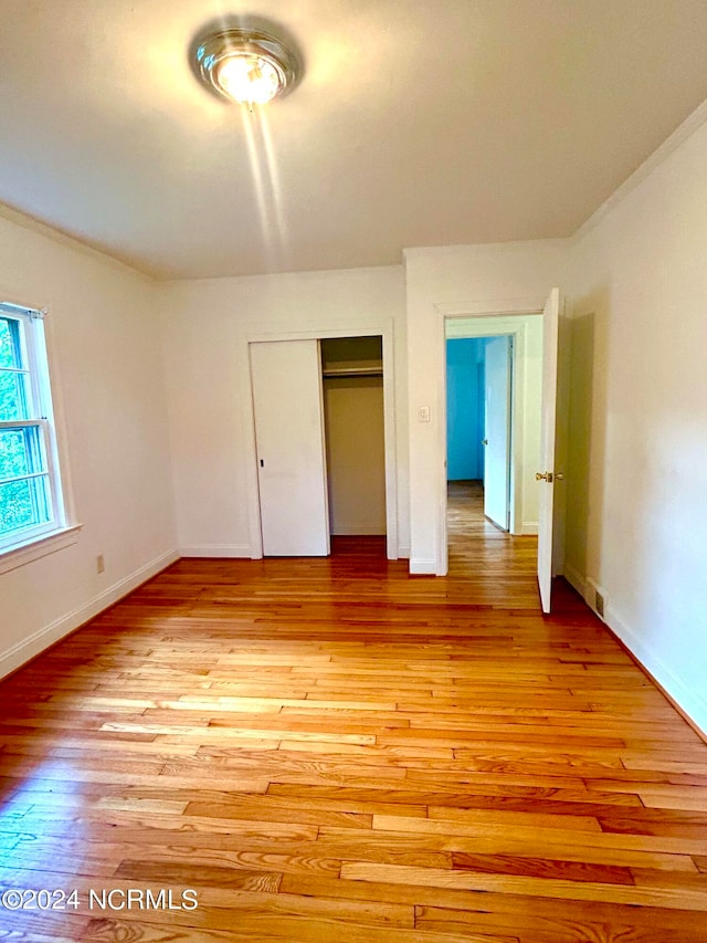 unfurnished bedroom with light wood-type flooring, crown molding, and a closet