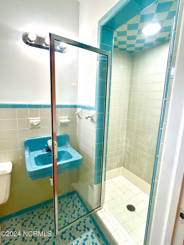 bathroom with tile patterned flooring, tile walls, toilet, and an enclosed shower