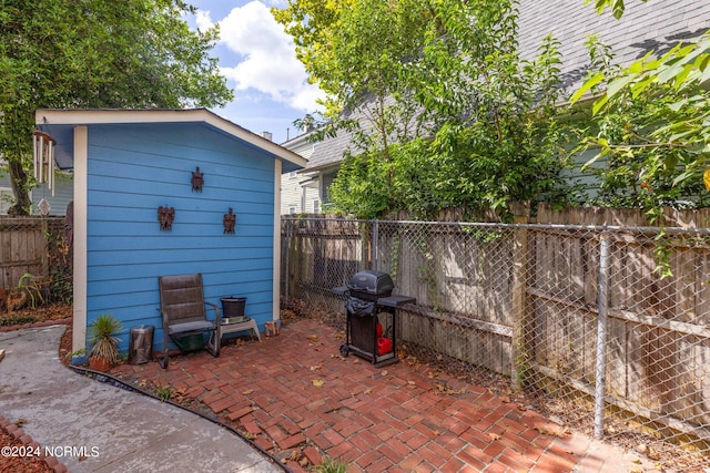 view of patio with a fenced backyard, a storage unit, grilling area, and an outbuilding