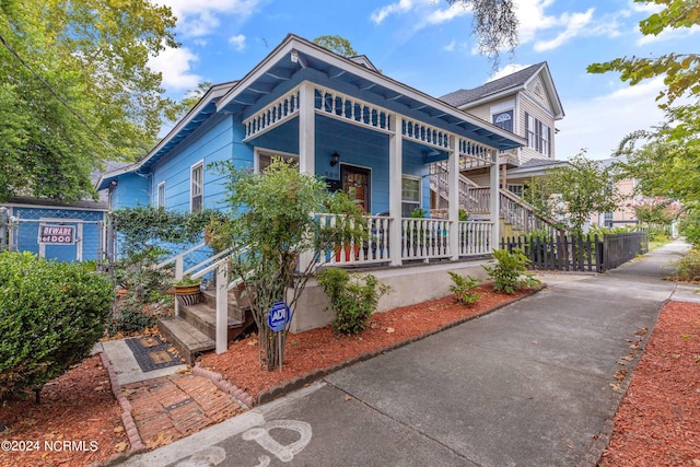 view of front of home with covered porch, fence, and stairway