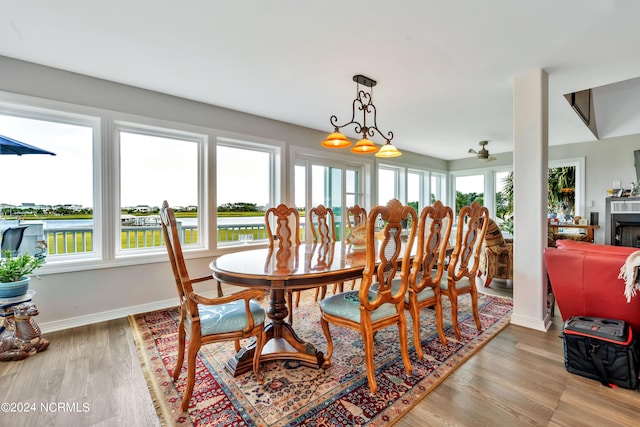 dining area with ceiling fan, a water view, and light wood-type flooring