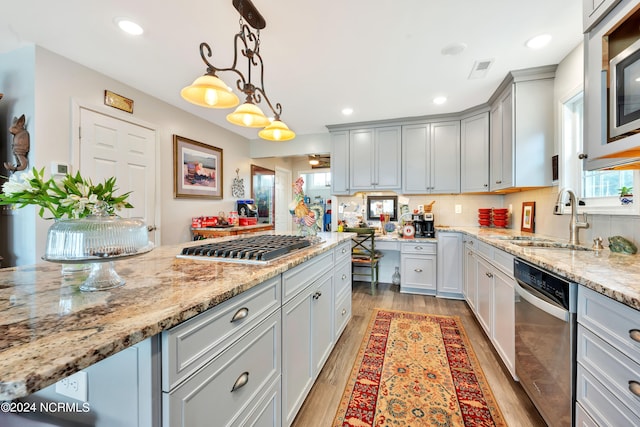 kitchen featuring light stone countertops, appliances with stainless steel finishes, sink, decorative light fixtures, and light hardwood / wood-style floors