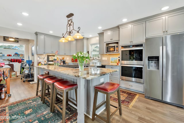 kitchen with a kitchen breakfast bar, gray cabinets, stainless steel appliances, and light hardwood / wood-style flooring