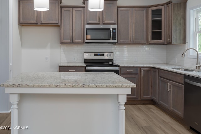 kitchen with light stone countertops, stainless steel appliances, sink, and light hardwood / wood-style flooring